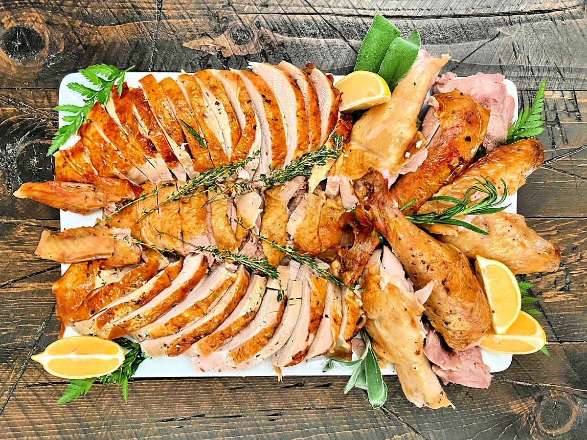 A carved holiday turkey on a white platter with rosemary and lemons around it