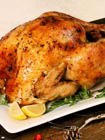 A holiday turkey on a white platter with rosemary and lemons around it