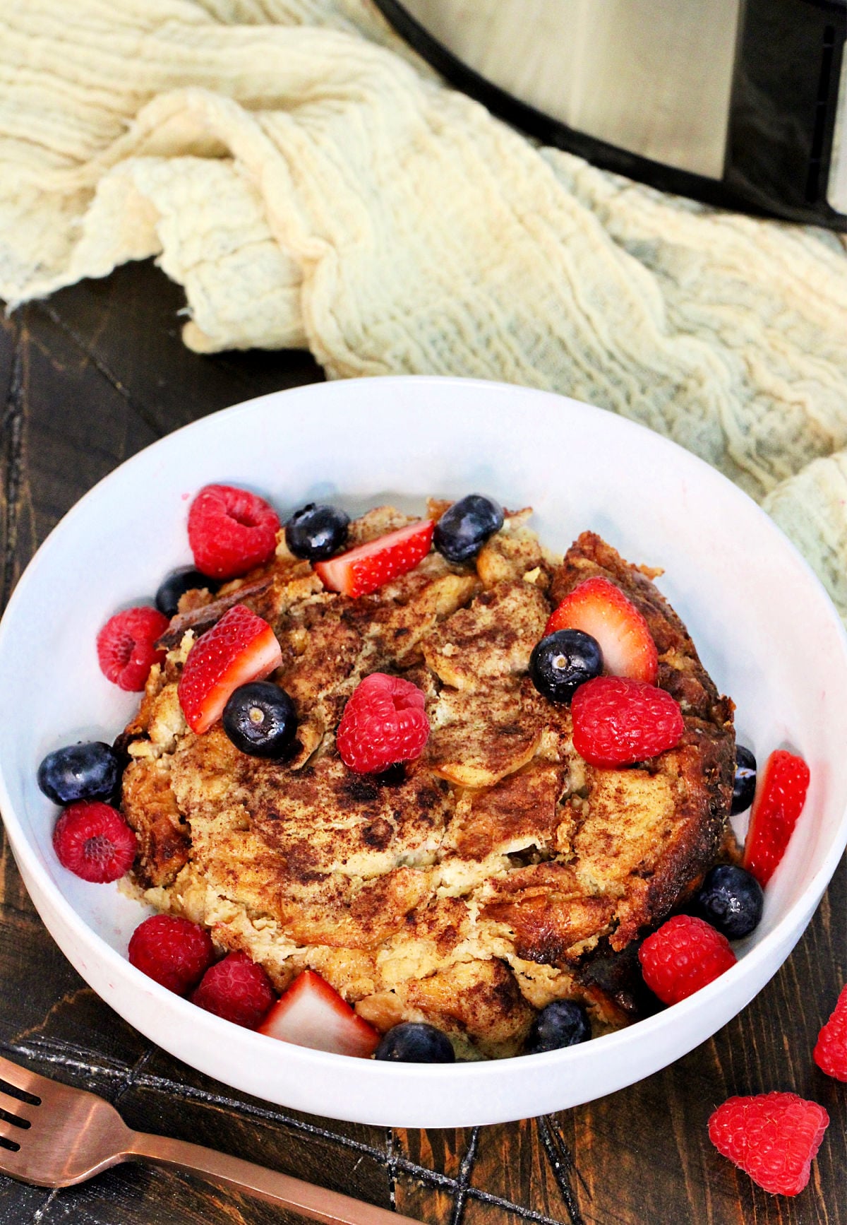 Crockpot French toast casserole in a white bowl with fresh berries on top.