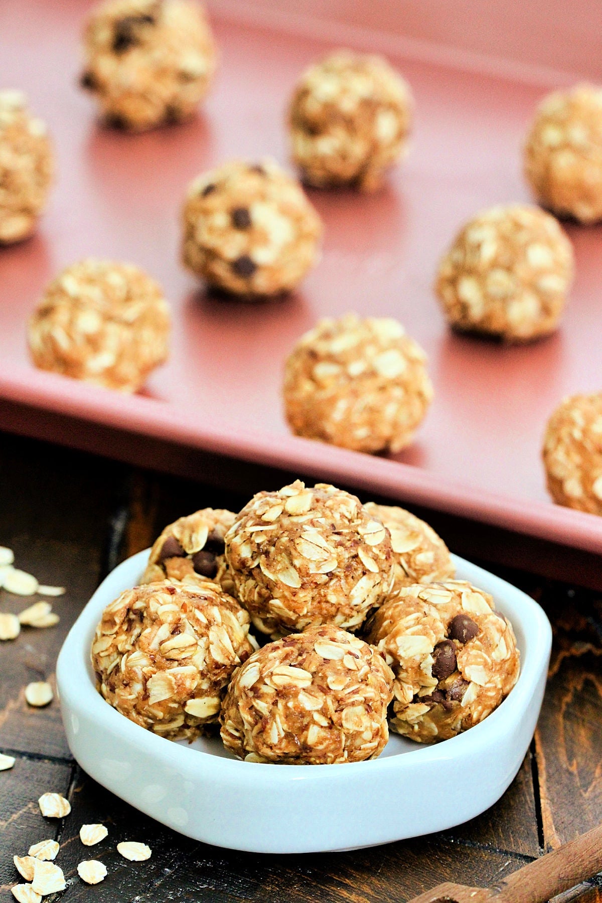 A stack of Peanut Butter Oatmeal Balls on a white dish in front of more balls on a pink baking sheet.