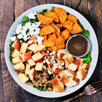 Harvest bowl with a side of vinaigrette in a white bowl on a wooden board.