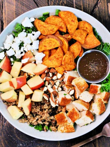 Harvest bowl with a side of vinaigrette in a white bowl on a wooden board.