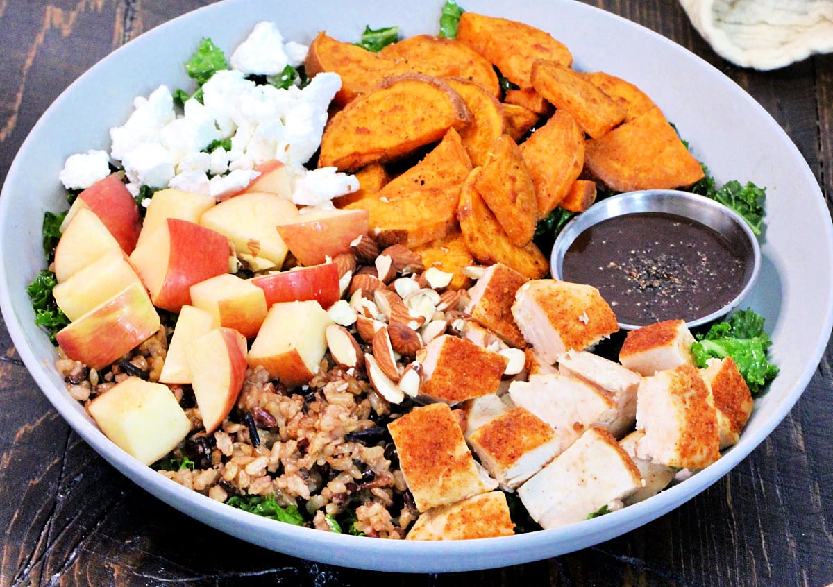 Harvest bowl with a side of vinaigrette in a white bowl on a wooden board.