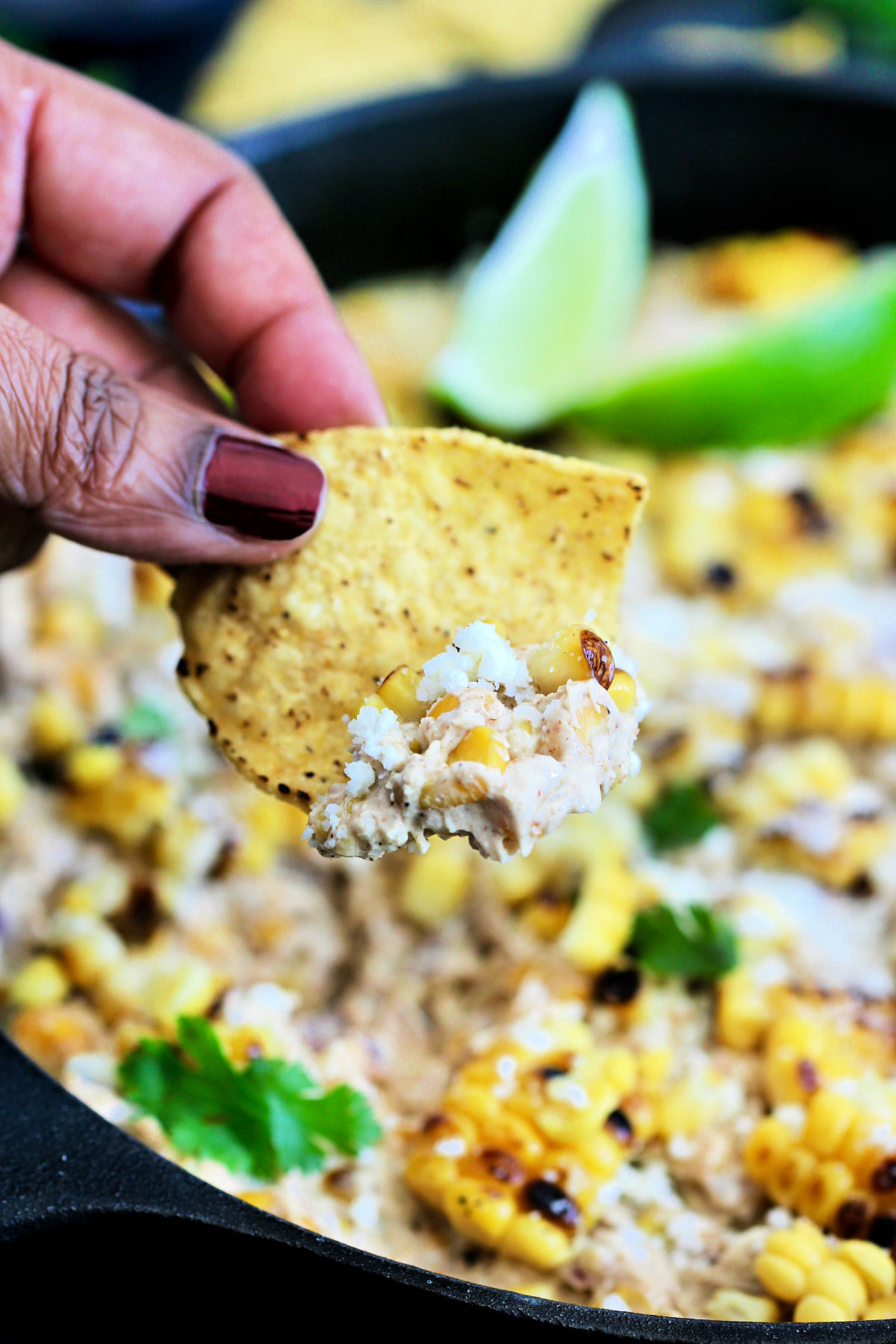 Fingers holding a tortilla chip with a scoop of Mexican street corn dip on it.