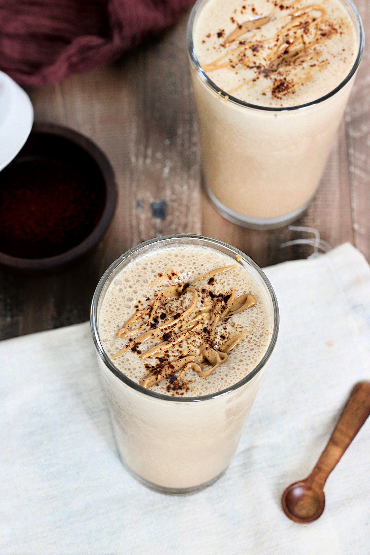 Two coffee protein smoothies on a wooden board with a white napkin and a wooden spoon.