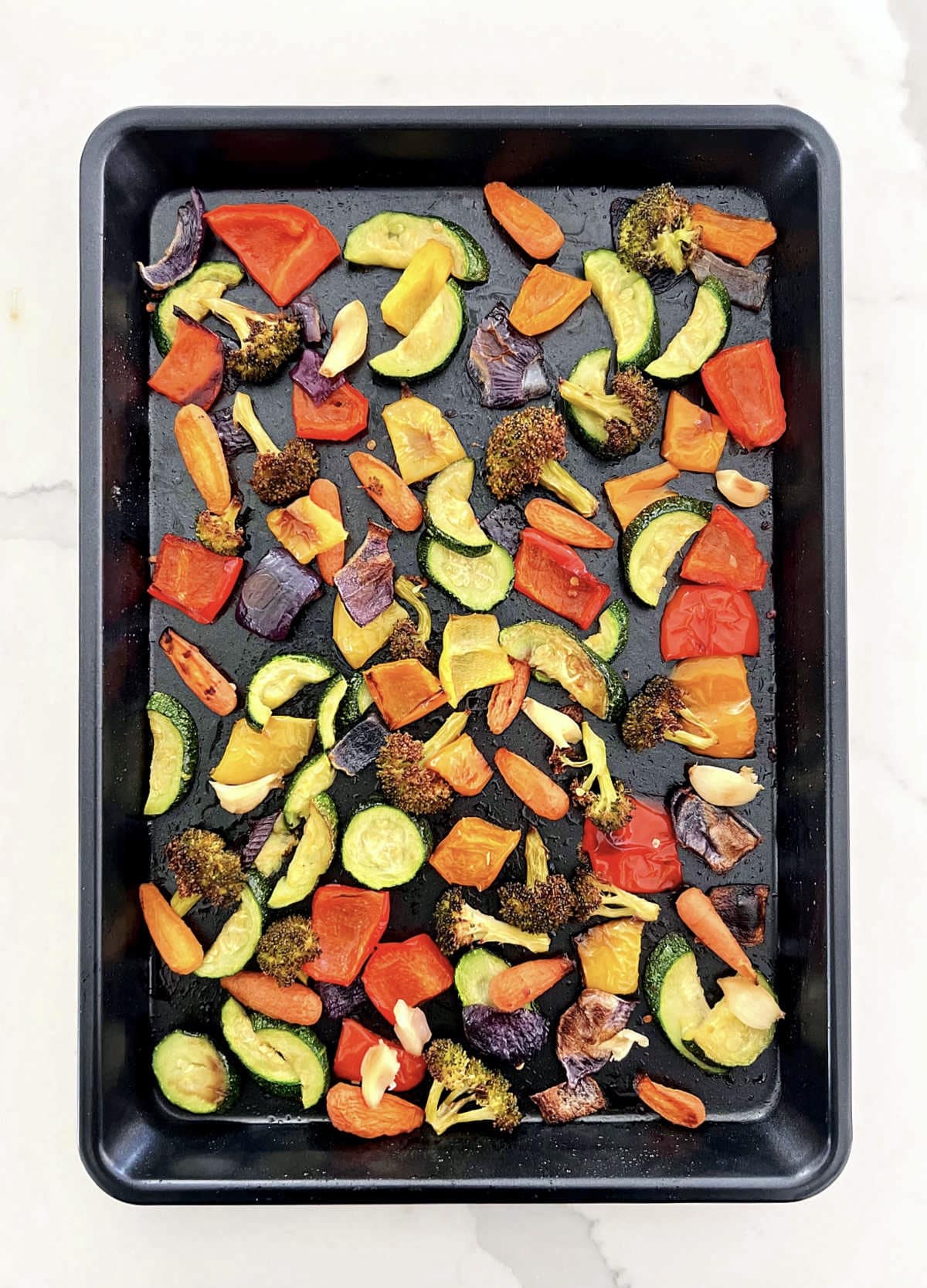 The perfect oven-roasted vegetables on a black sheet pan.