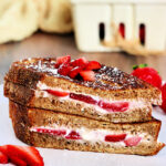 Two pieces of strawberry stuffed French toast stacked on a white plate.
