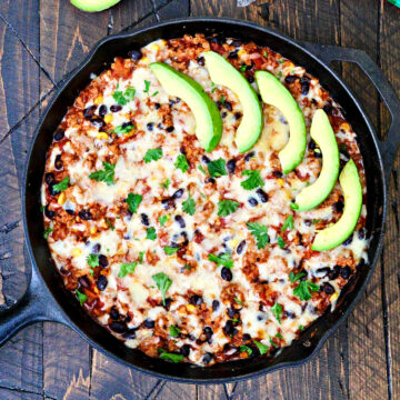 Turkey Taco Skillet garnished with slices of avocado in a cast iron skillet on a wooden board.