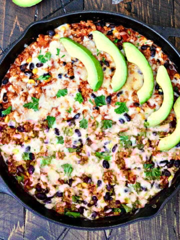 Turkey Taco Skillet garnished with slices of avocado in a cast iron skillet on a wooden board.