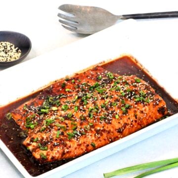 Honey ginger salmon in a white serving platter with sesame seeds and a silver serving utensil in the background.