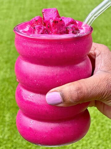 Dragon fruit smoothie in a bubble glass being held outside.