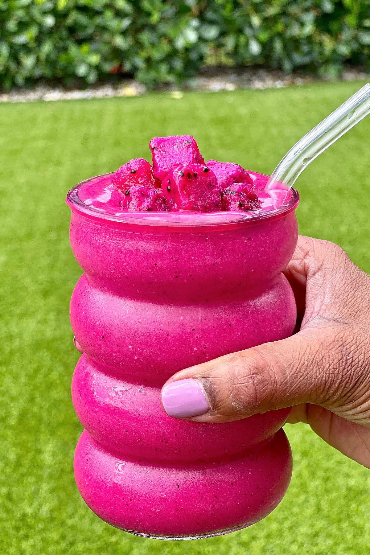 Dragon fruit smoothie in a bubble glass being held outside.