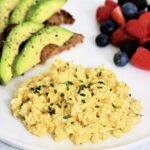 High protein scrambled eggs with cottage cheese on white plate with avocado toast and mixed berries