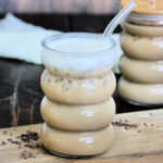 A glass of protein iced coffee with a glass straw and another glass in the background.