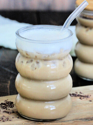 A glass of protein iced coffee with a glass straw and another glass in the background.