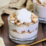 Cottage Cheese Banana Pudding in a glass on a wooden board with a gold spoon and tan napkin nearby.