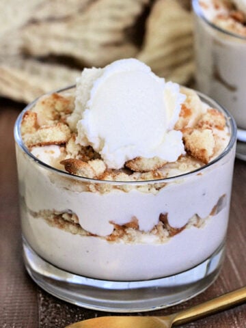 Cottage Cheese Banana Pudding in a glass on a wooden board with a gold spoon and tan napkin nearby.