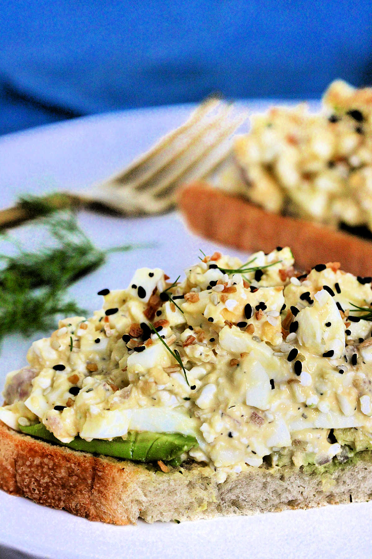 Two slices of bread topped with cottage cheese egg salad on a white plate with dill and a fork nearby.