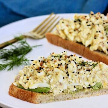 Two slices of bread topped with cottage cheese egg salad on a white plate with dill and a fork nearby.