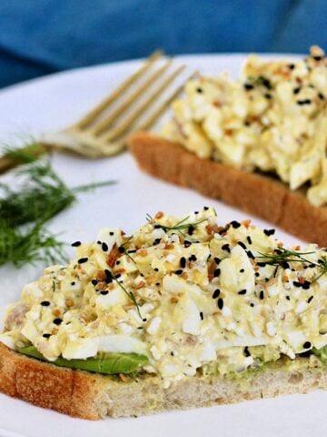 Two slices of bread topped with cottage cheese egg salad on a white plate with dill and a fork nearby.