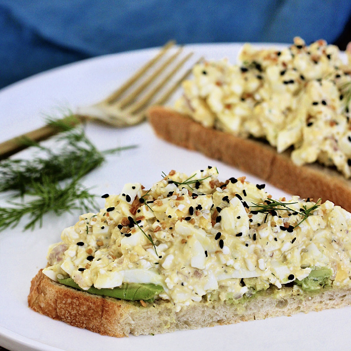Two slices of bread topped with cottage cheese egg salad on a white plate with dill and a fork nearby.