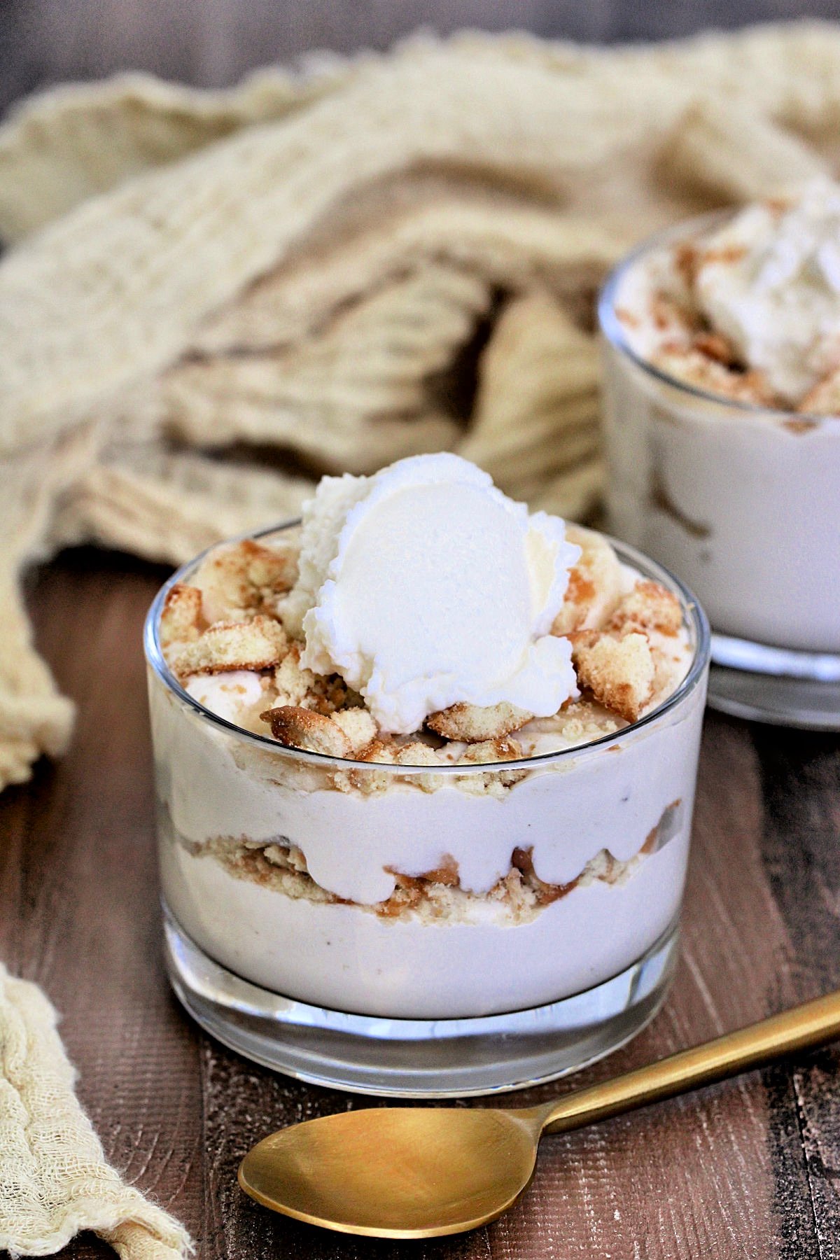 Cottage Cheese Banana Pudding in a glass on a wooden board with a gold spoon and tan napkin nearby.