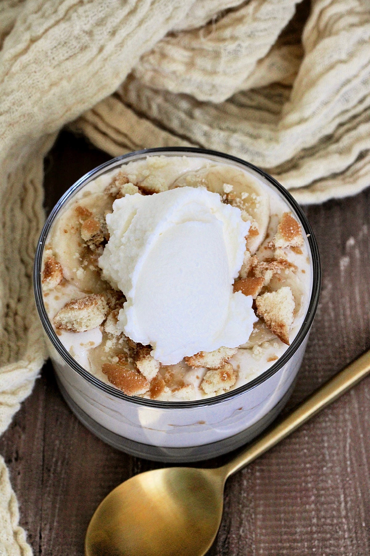 Cottage Cheese Banana Pudding in a glass on a wooden board with a gold spoon and tan napkin nearby.