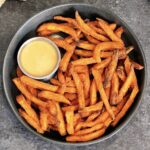 A bowl of air fryer sweet potato fries with a cup of dipping sauce.