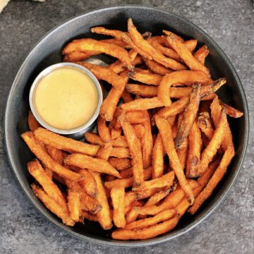 A bowl of air fryer sweet potato fries with a cup of dipping sauce.