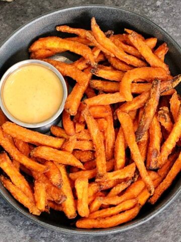 A bowl of air fryer sweet potato fries with a cup of dipping sauce.