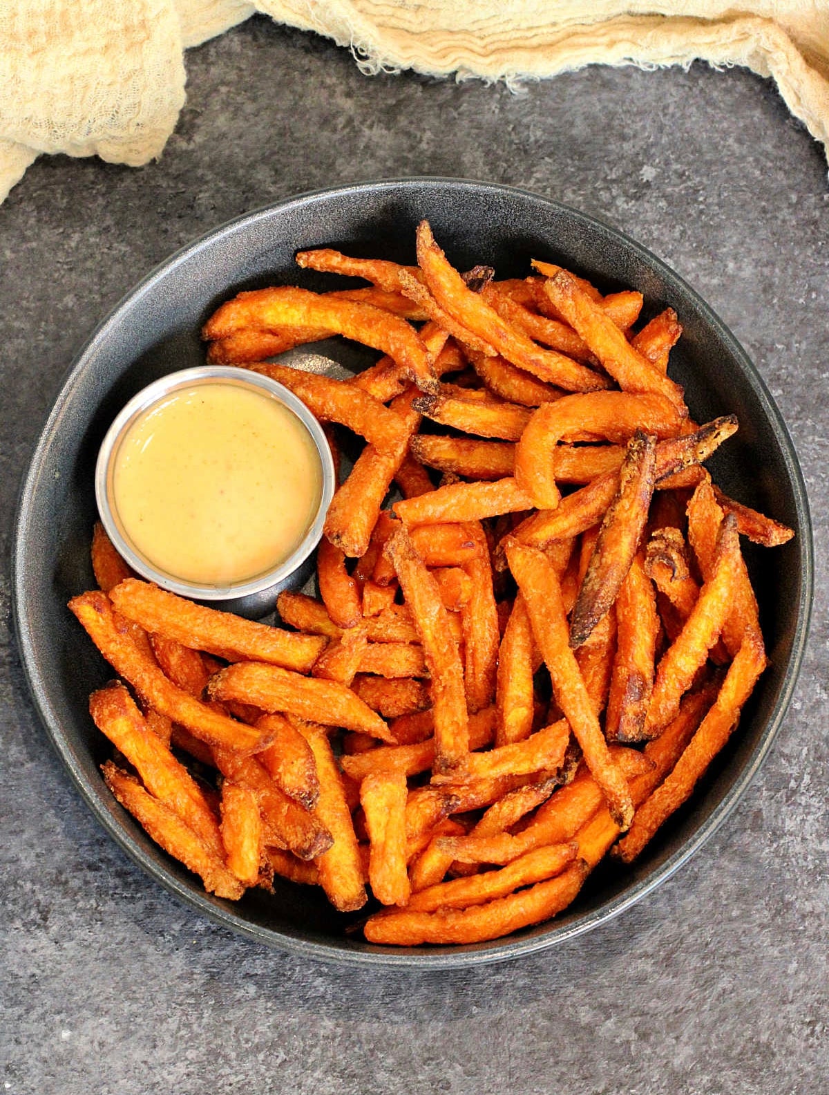 A bowl of air fryer sweet potato fries with a cup of dipping sauce.