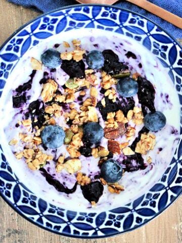 Blueberry chia jam swirled into a bowl of Greek yogurt topped with fresh blueberries and granola.