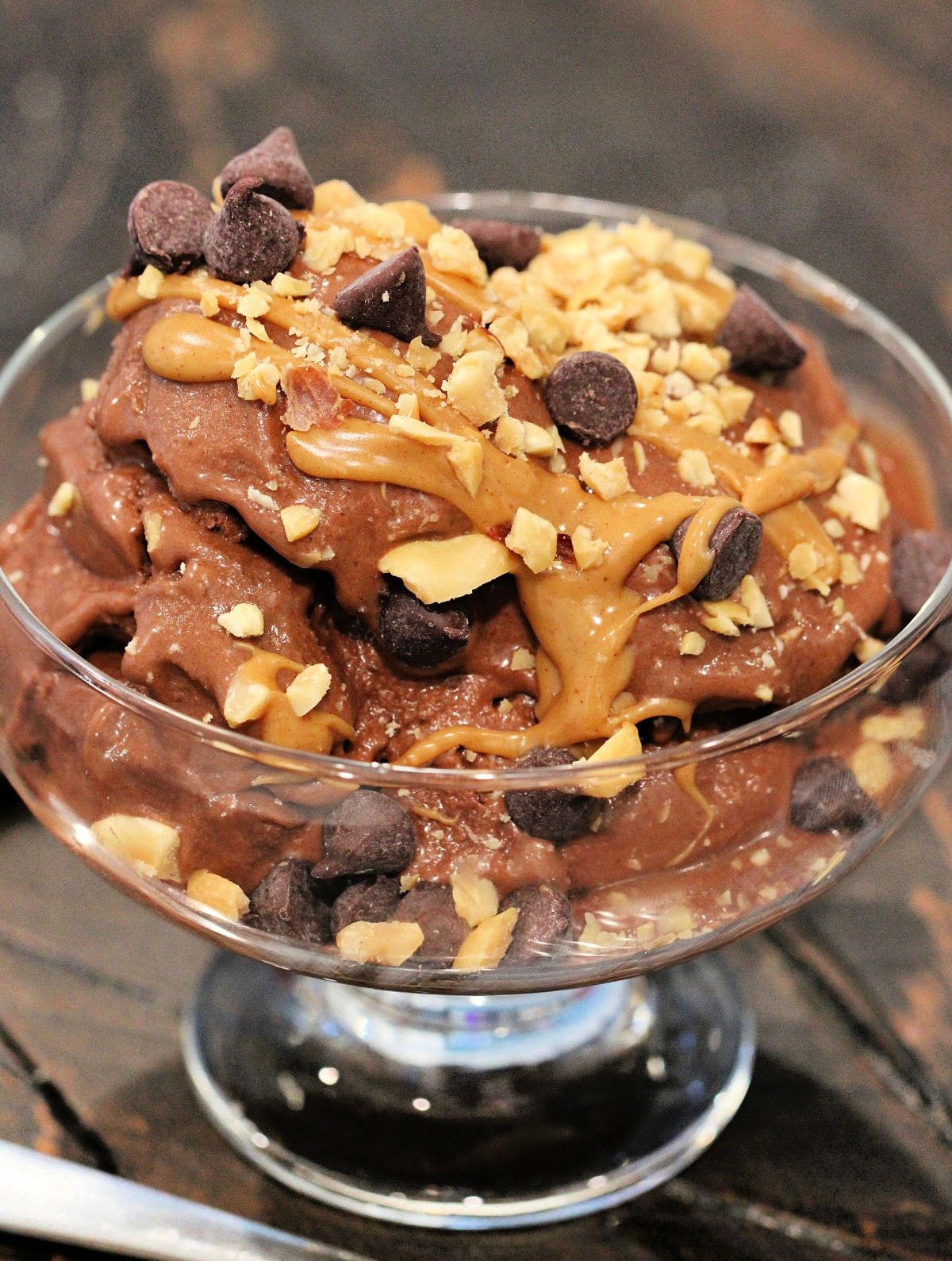 Healthy chocolate banana "ice cream" in a glass bowl topped with peanut butter, chocolate chips and crushed peanuts.