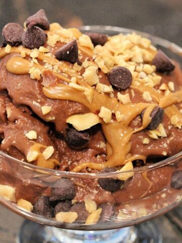 Healthy chocolate banana "ice cream" in a glass bowl topped with peanut butter, chocolate chips and crushed peanuts.