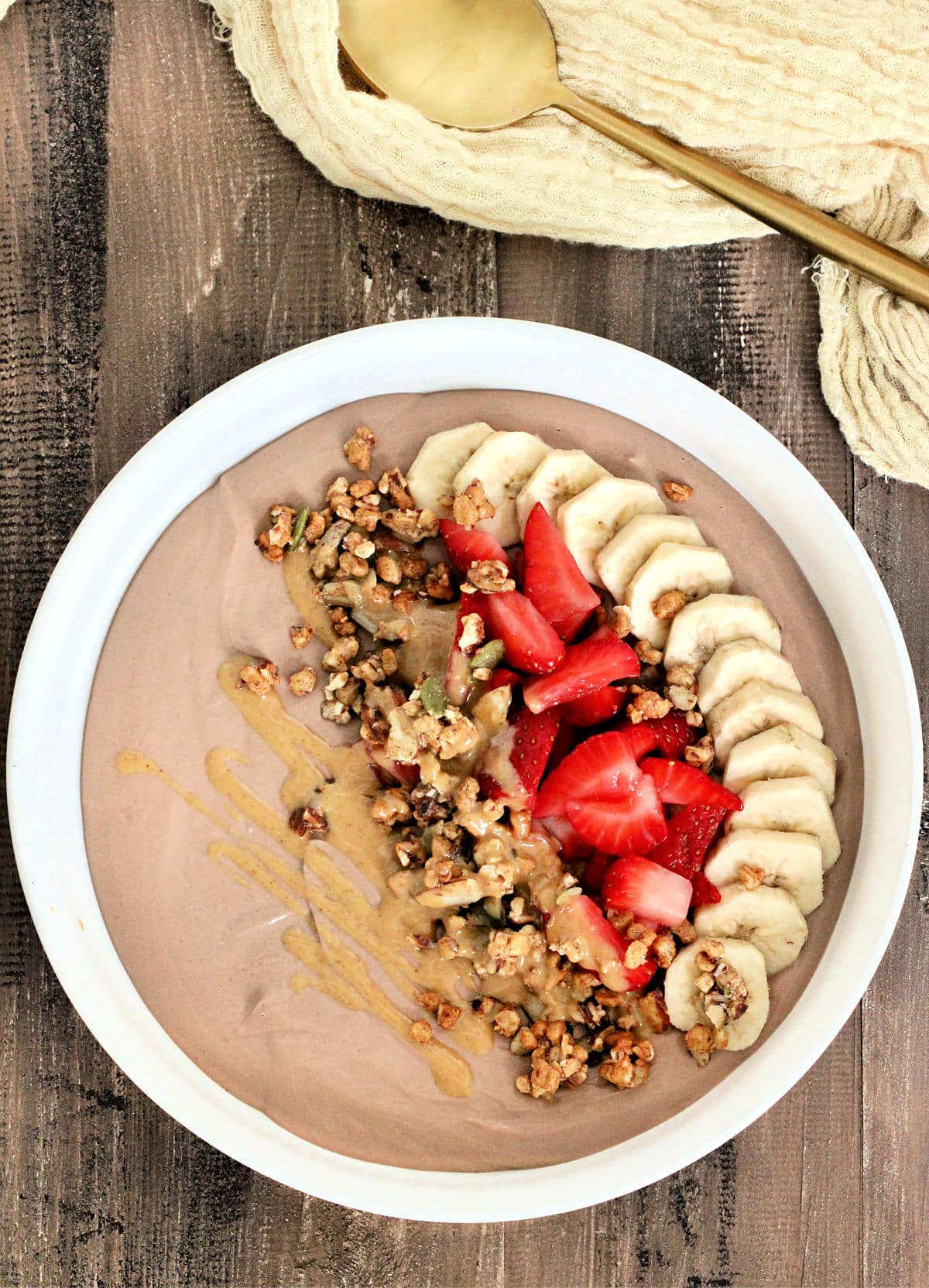Chocolate protein yogurt bowl topped with banana, strawberry, granola and peanut butter.