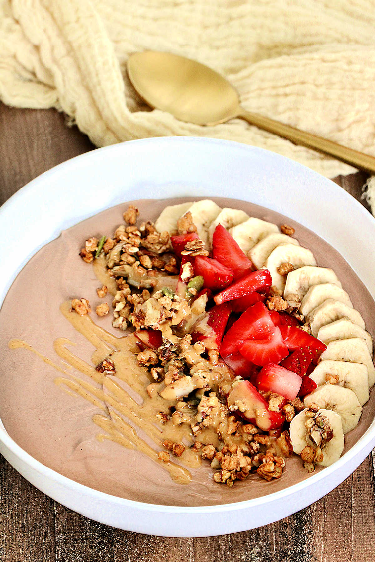 Chocolate protein yogurt bowl topped with banana, strawberry, granola and peanut butter.