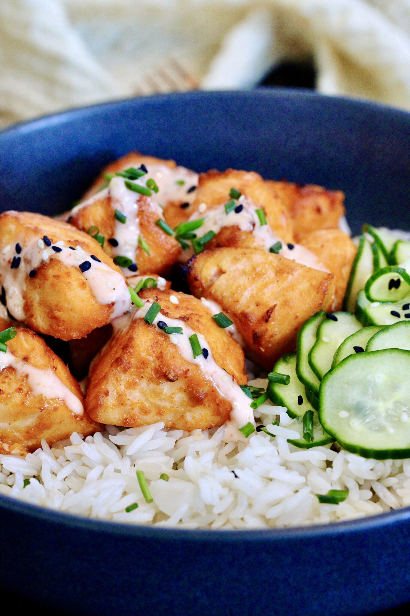 Bang Bang Salmon Bites with pickled cucumbers on a bed of white rice in a black bowl.