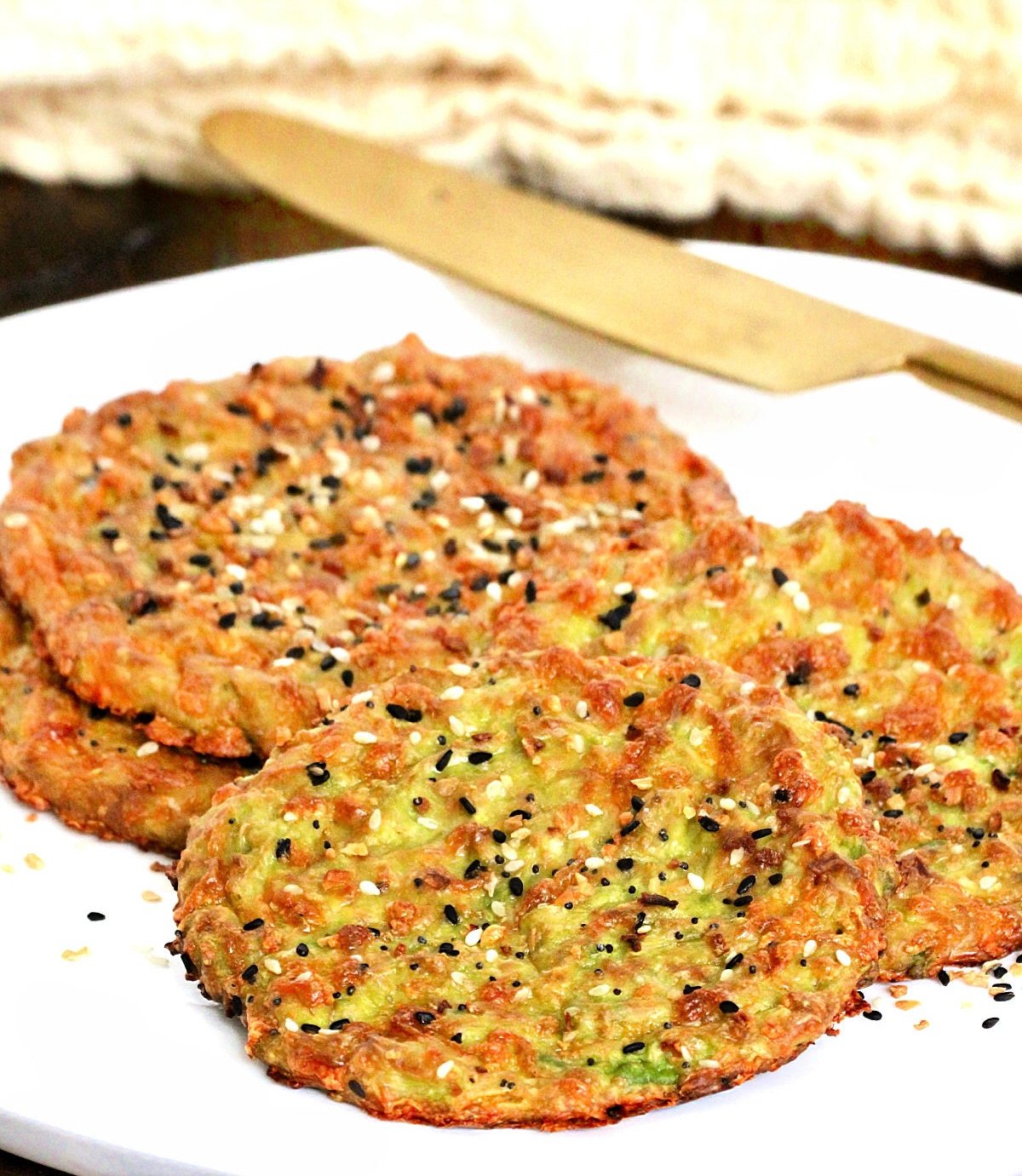 Pieces of avocado bread on a white plate with a gold knife and beige napkin in background.