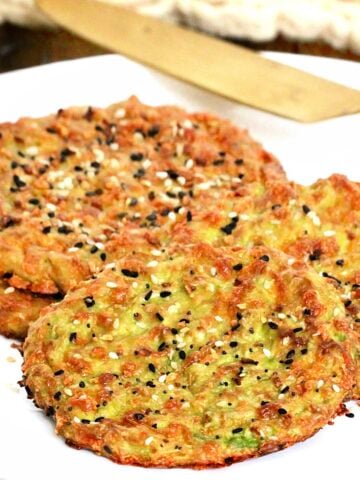 Pieces of avocado bread on a white plate with a gold knife and beige napkin in background.
