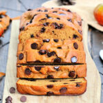 A loaf of high protein pumpkin chocolate chip bread on a wooden board cut into several slices.