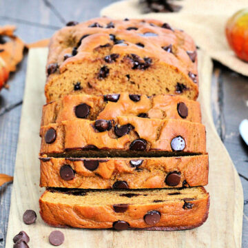 A loaf of high protein pumpkin chocolate chip bread on a wooden board cut into several slices.