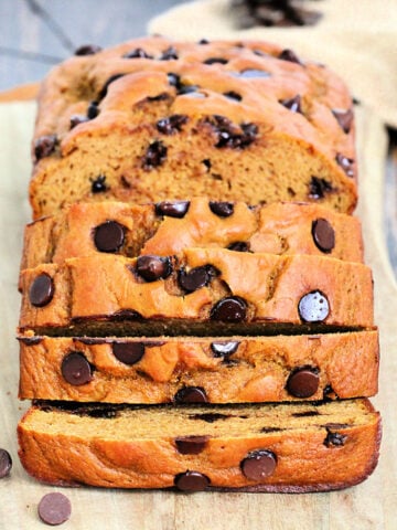 A loaf of high protein pumpkin chocolate chip bread on a wooden board cut into several slices.