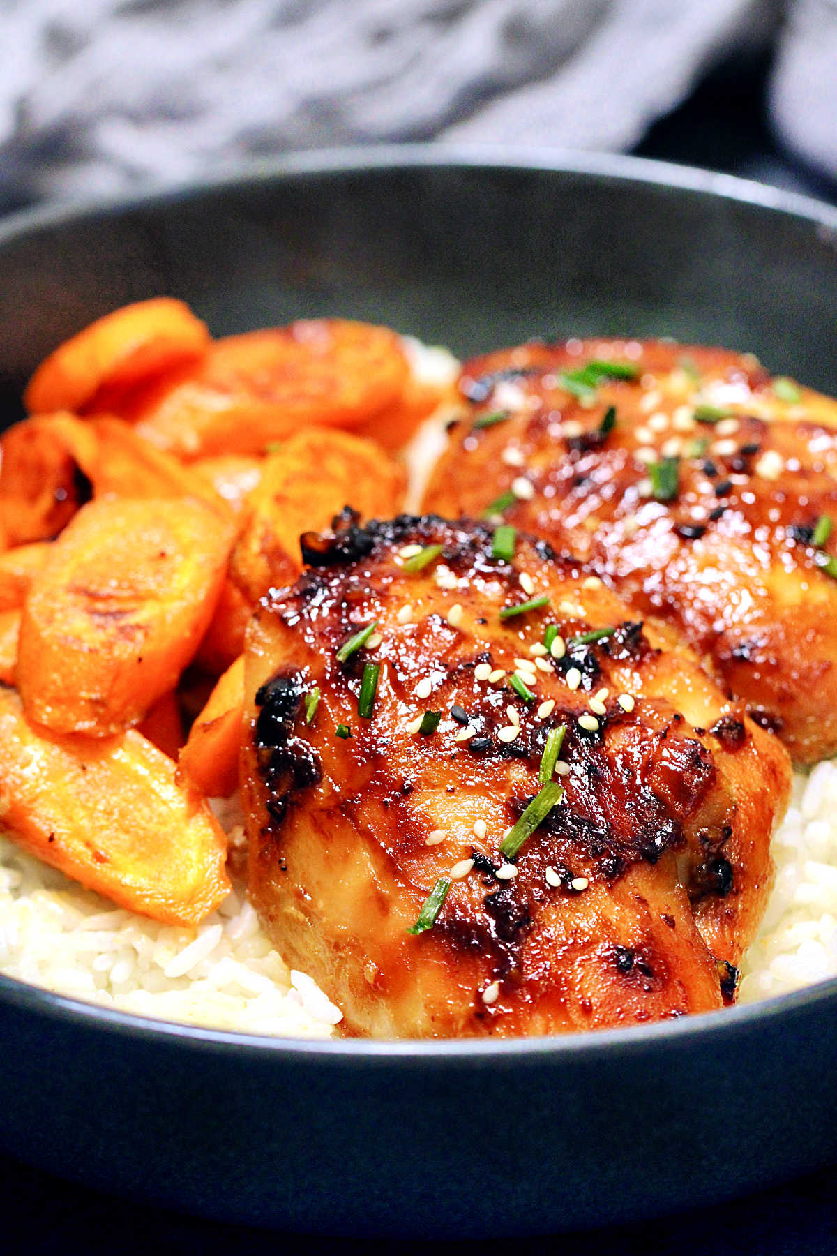 Miso chicken thighs with roasted carrots and white rice in a black bowl.