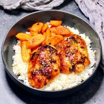 Miso chicken thighs with roasted carrots and white rice in a black bowl.