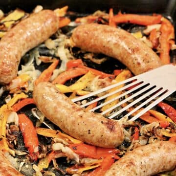 Baked sausage and peppers on sheet pan with spatula.