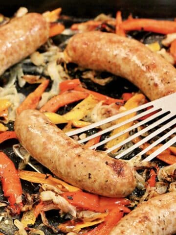 Baked sausage and peppers on sheet pan with spatula.