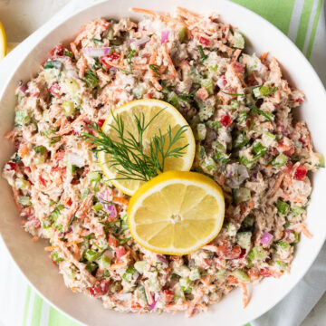 Canned salmon salad in a white bowl garnished with lemon slices and dill.