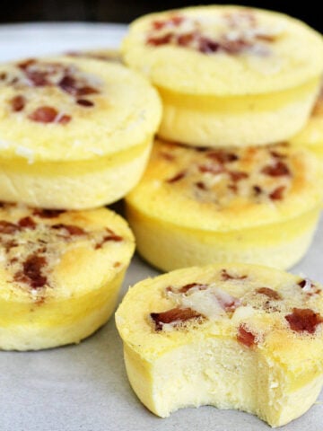 A stack of Starbucks copycat egg bites with bacon on a plate, one has a bite taken out of it.