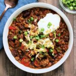 Bowl of hearty pumpkin chili topped with cheese, sour cream and scallions