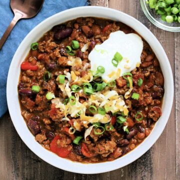Bowl of hearty pumpkin chili topped with cheese, sour cream and scallions